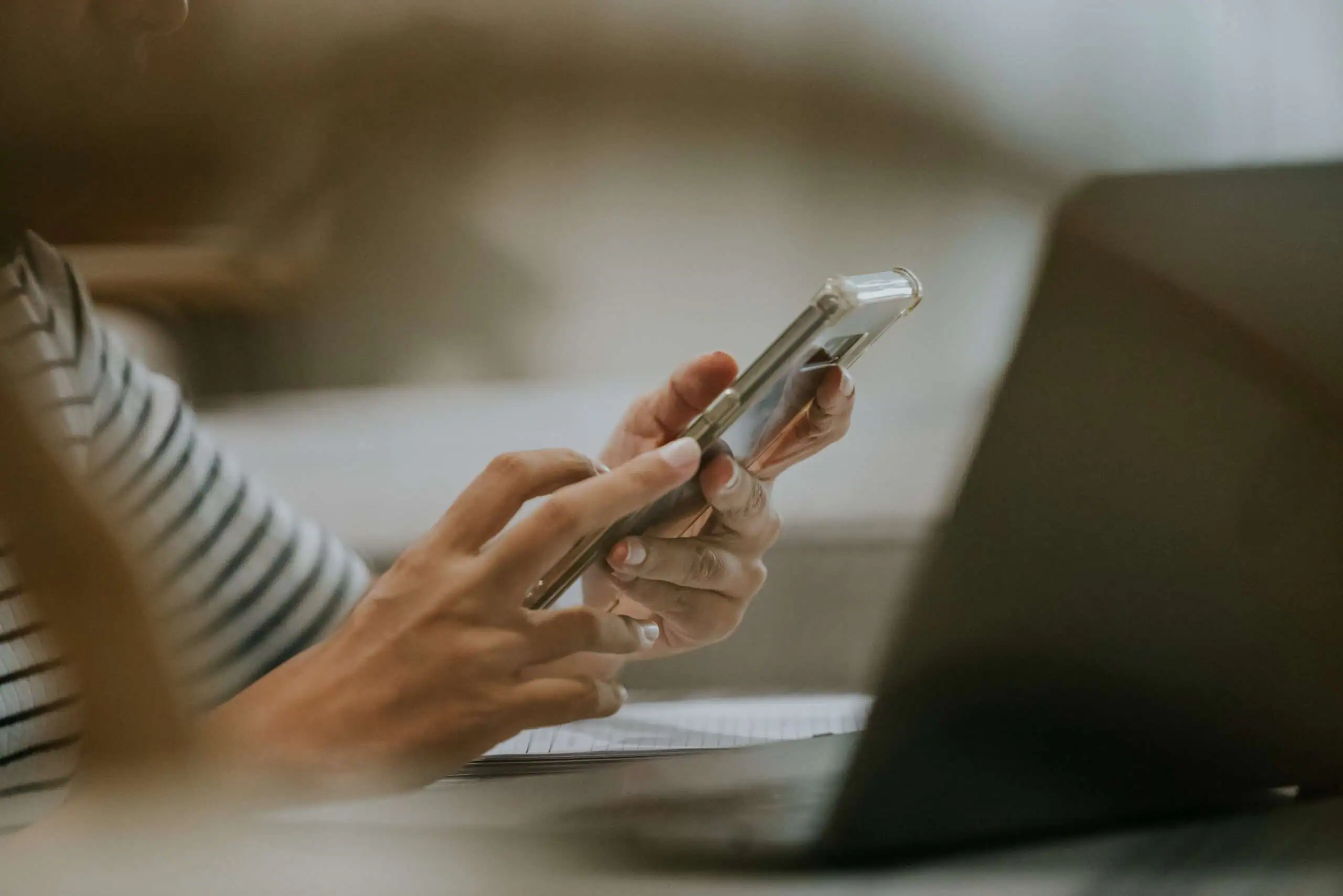 A woman holding a mobile phone in front a laptop